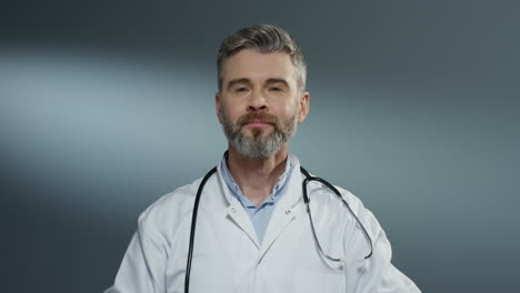 Portrait-of-the-Caucasian-joyful-handsome-male-doctor-taking-off-blue-mask-from-his-mouth-and-smiling-to-the-camera.-Close-up.